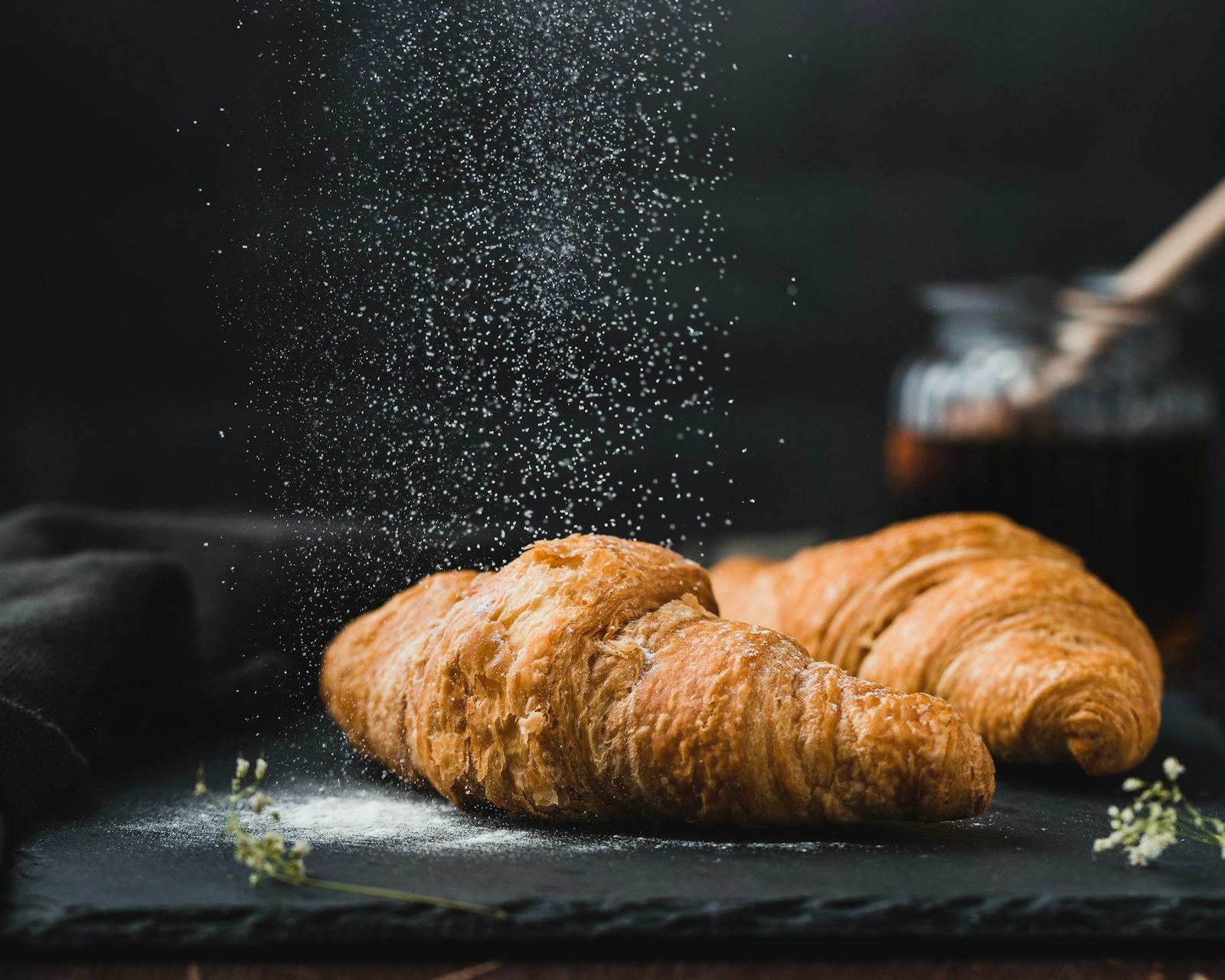 Powdered sugar falling over a fresh croissant on a dark surface