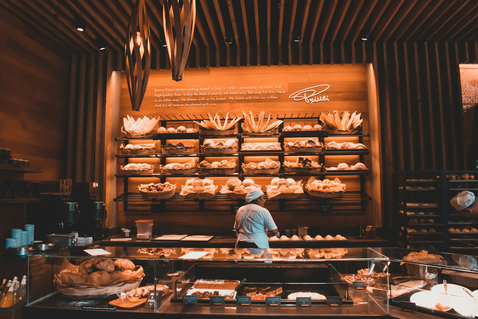 A baker arranging fresh bread inside a warm, wood-lined bakery